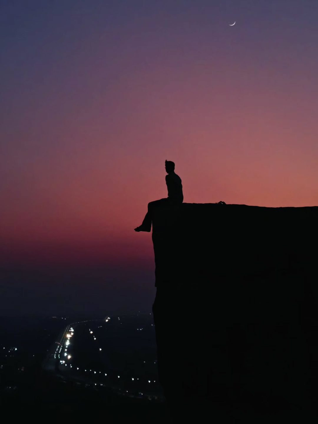 Silhouette sitting on a cliff edge at twilight