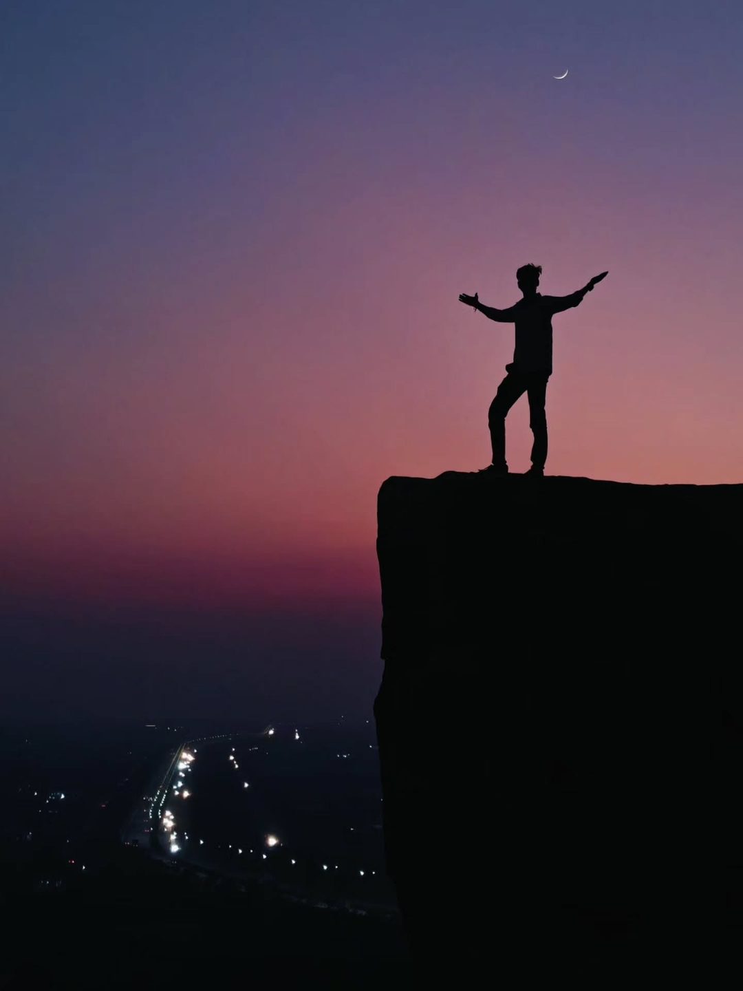 Silhouette with open arms at dusk above the city lights