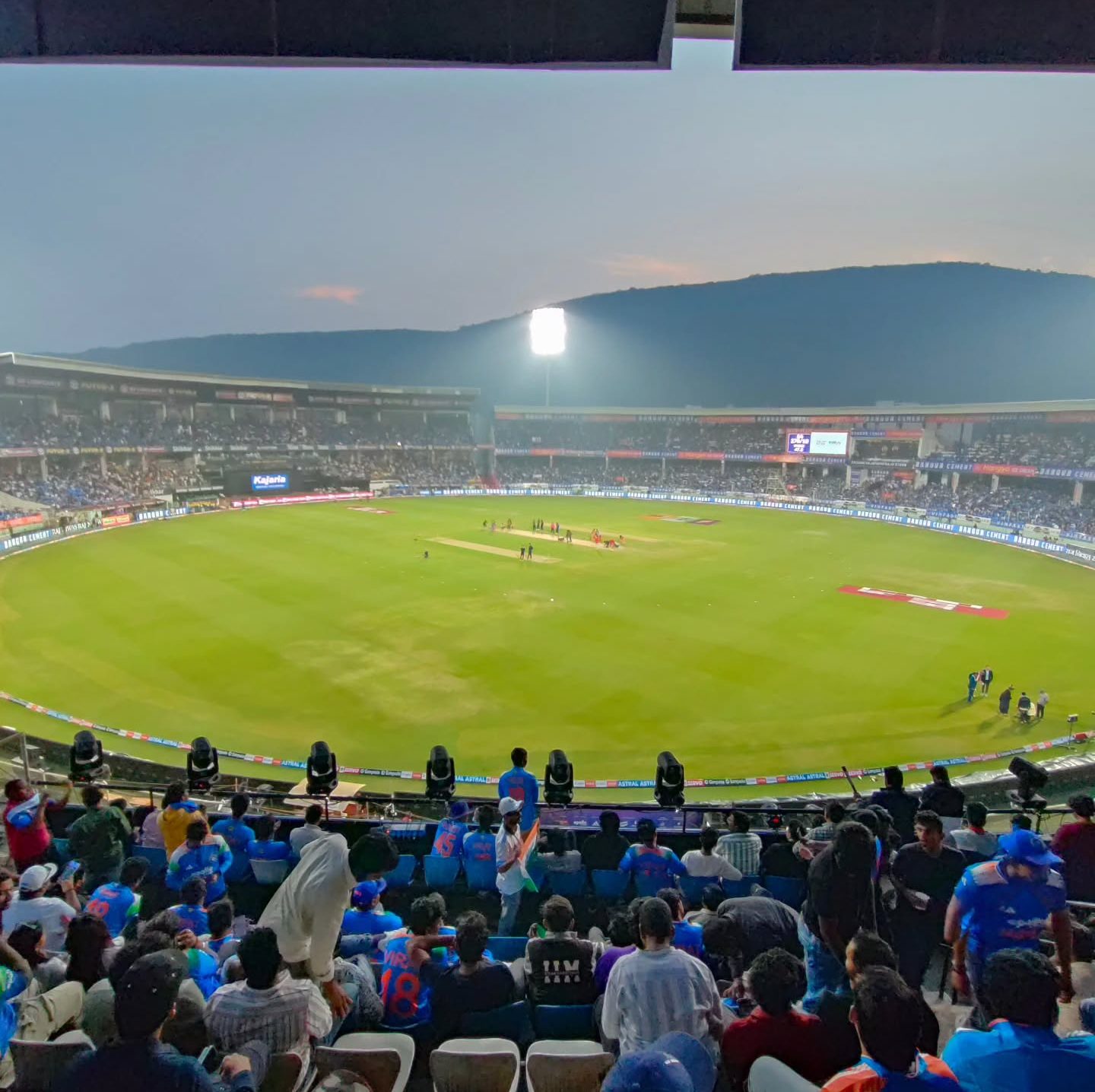 Packed floodlit cricket stadium on match night, by Sai Clicks